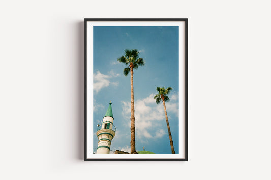 Framed artwork of a minaret and palm trees against a blue sky.