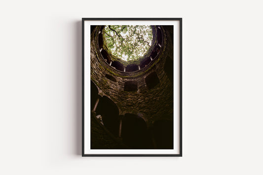 Framed photograph of a stone well with a view of trees at the top.