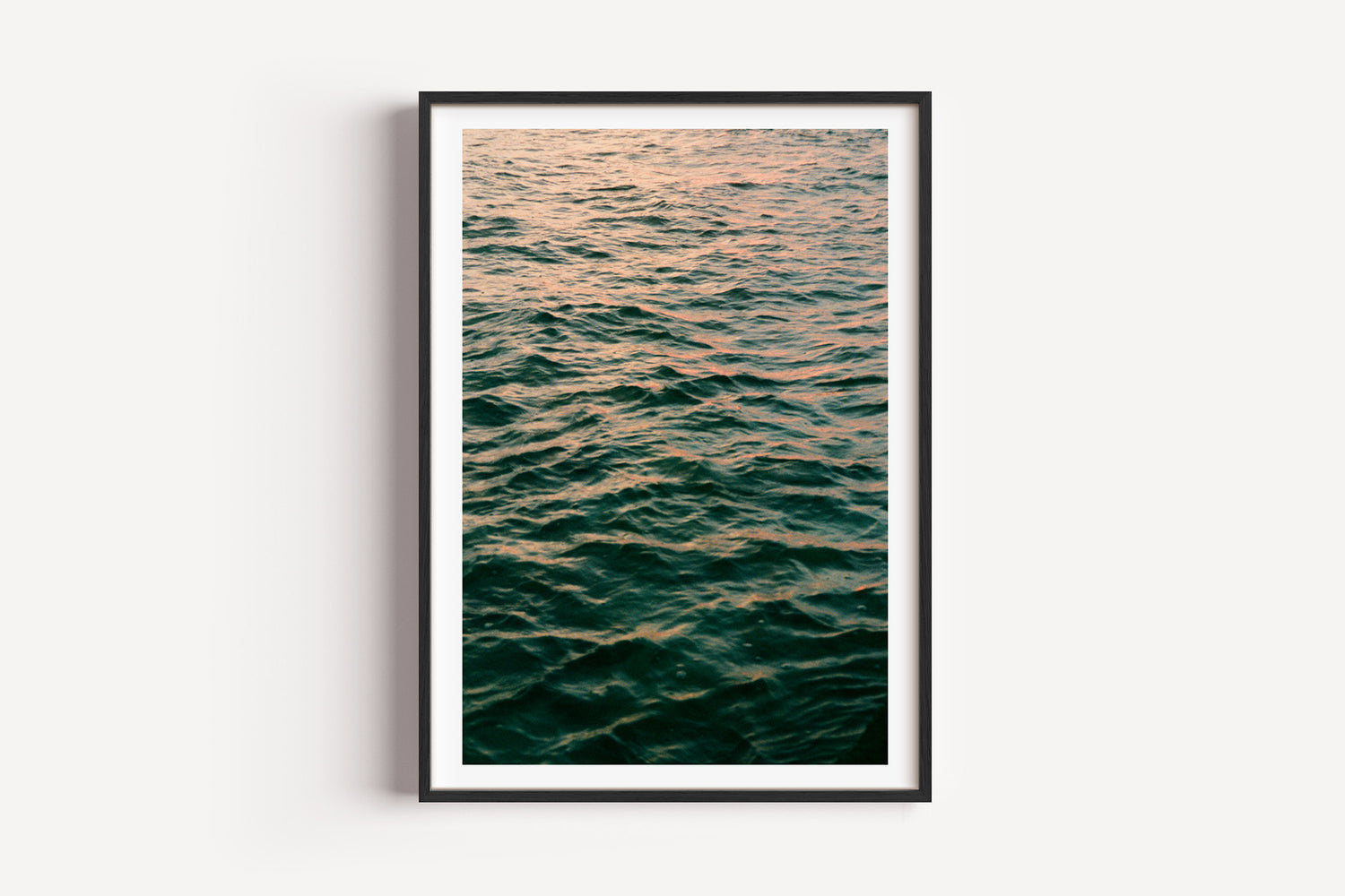 Framed photograph of a sunset over water on a white wall