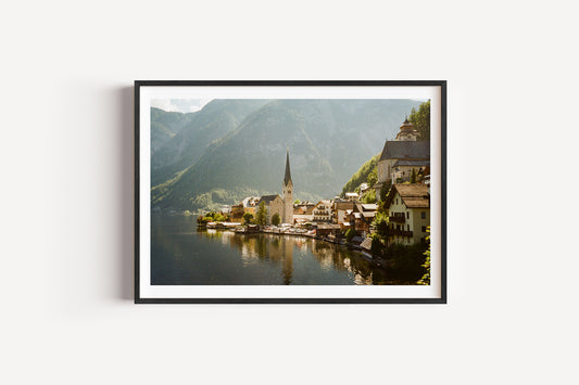 Framed photograph of a scenic village by a lake with mountains in the background.