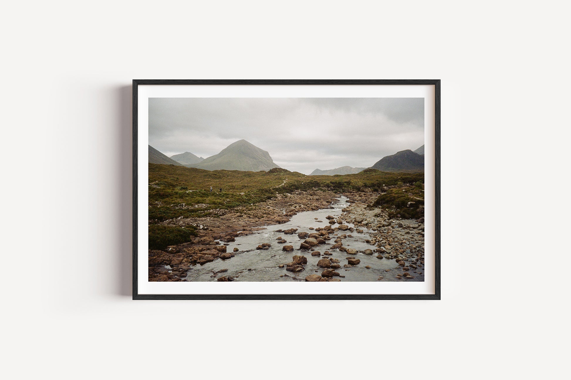 Framed photograph of a mountain landscape with a stream on a white wall
