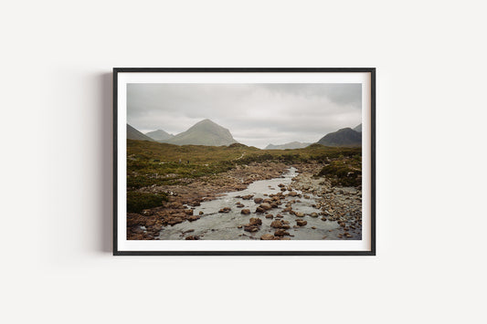 Framed photograph of a mountain landscape with a stream on a white wall
