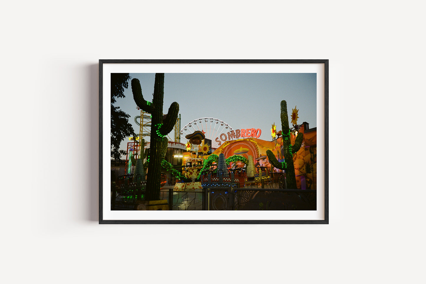 Framed photograph of a nighttime scene with cacti and a neon sign on a white wall.